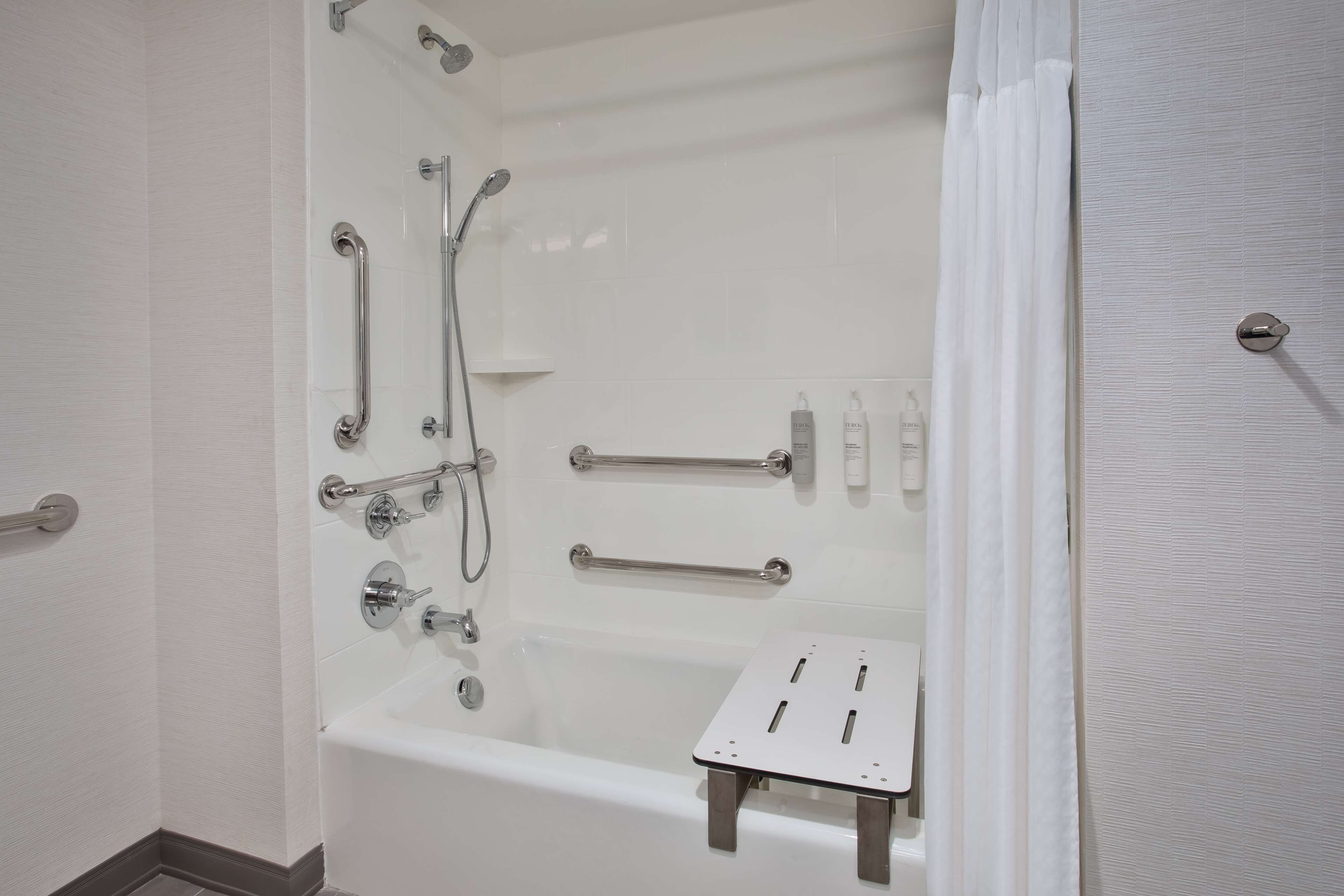 A modern bathroom with a bathtub, shower, and grab bars.