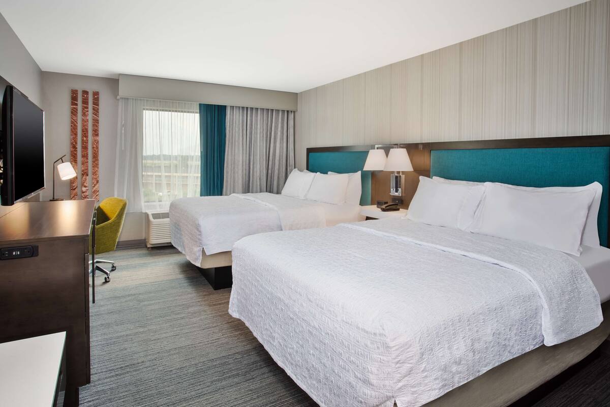 A hotel room with two beds, a desk, a chair, a TV, and a window with curtains.