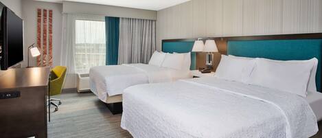 A hotel room with two beds, a desk, a chair, a TV, and a window with curtains.