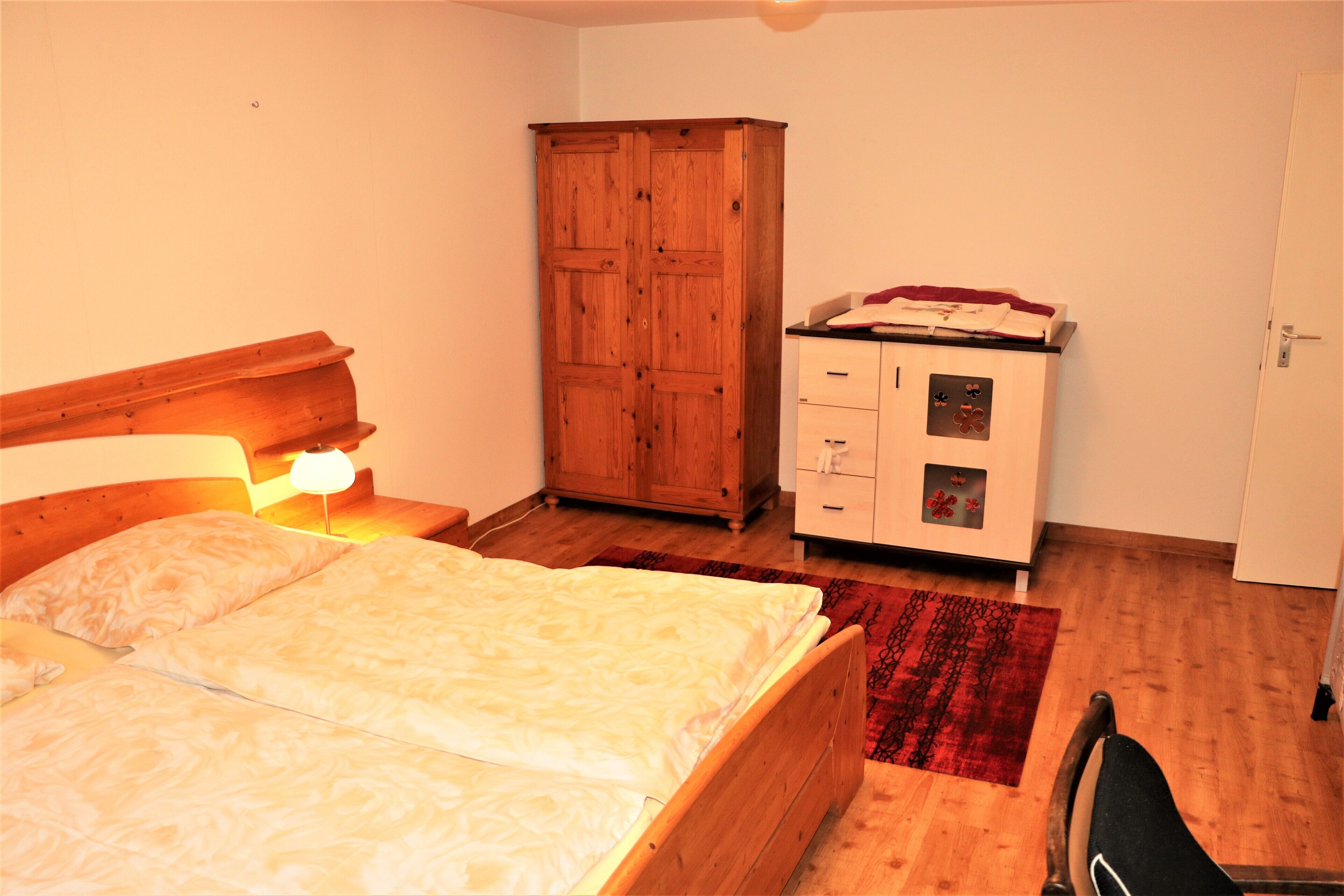 A bedroom with a wooden bed, a wardrobe, a dresser, and a red rug.