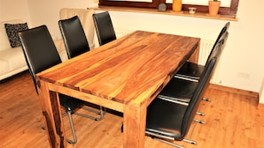 Une table à manger en bois, des chaises noires, un radiateur blanc et une fenêtre ornée de plantes.