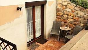 Un petit espace extérieur aménagé avec une table et deux chaises, un mur en pierre et une porte avec des rideaux.
