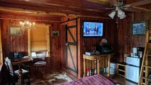 Een knus houten interieur met een houten plafond, een aan de muur bevestigde televisie, een bureau met stoel en een bed met een paarse deken.