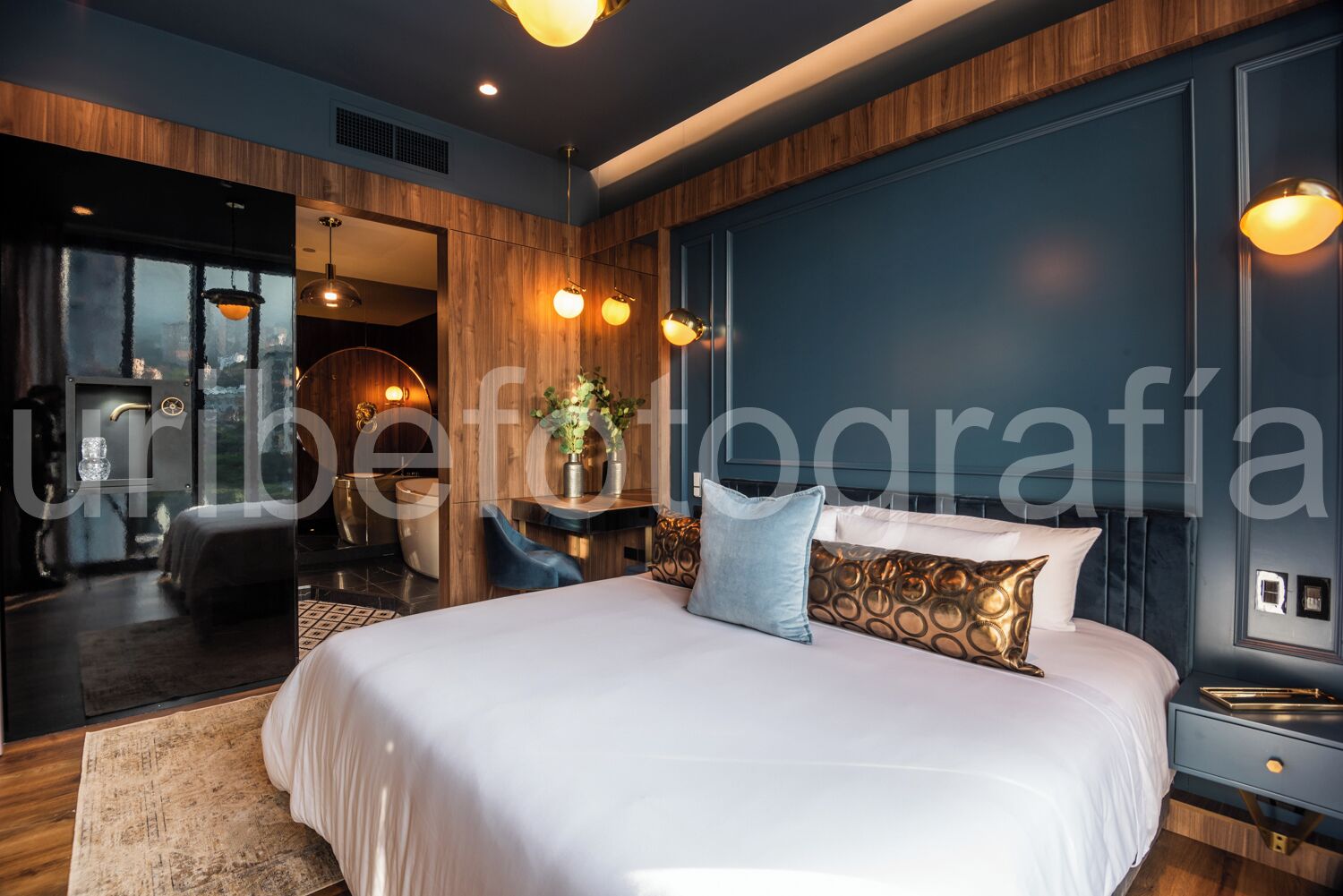 A modern bedroom with a large bed, wooden paneling, and a view of a cityscape through a large window.