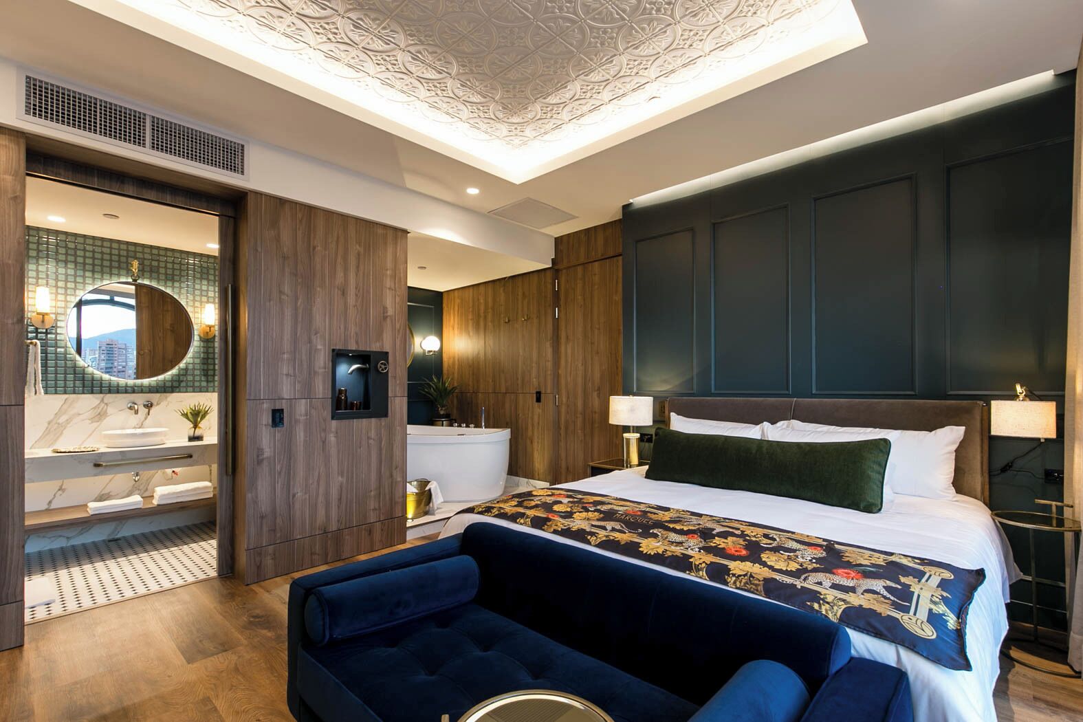 Una habitación de hotel moderna con una cama grande, una tocador con espejo, una bañera y un sillón tapizado en azul.