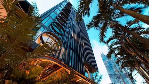 Un moderno edificio de gran altura con fachada de vidrio curva, rodeado de palmeras.