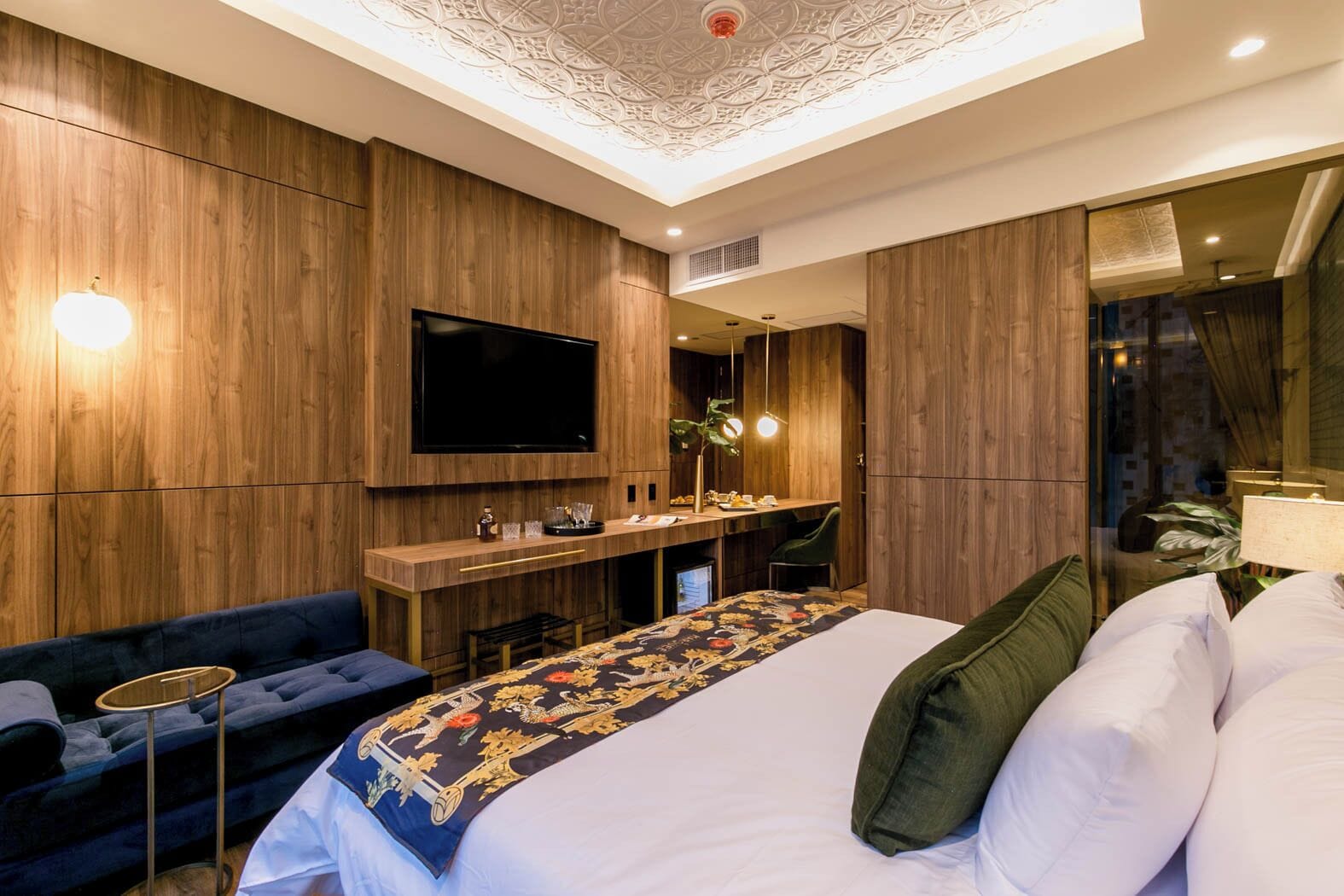 A modern hotel room with a large bed, a TV, a desk, and a seating area.