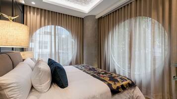 A modern bedroom with a bed, a lamp, and large windows with curtains.