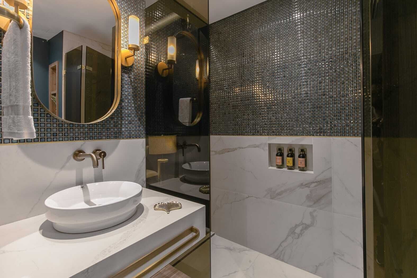 A modern bathroom with a white sink, gold fixtures, and a mirror.