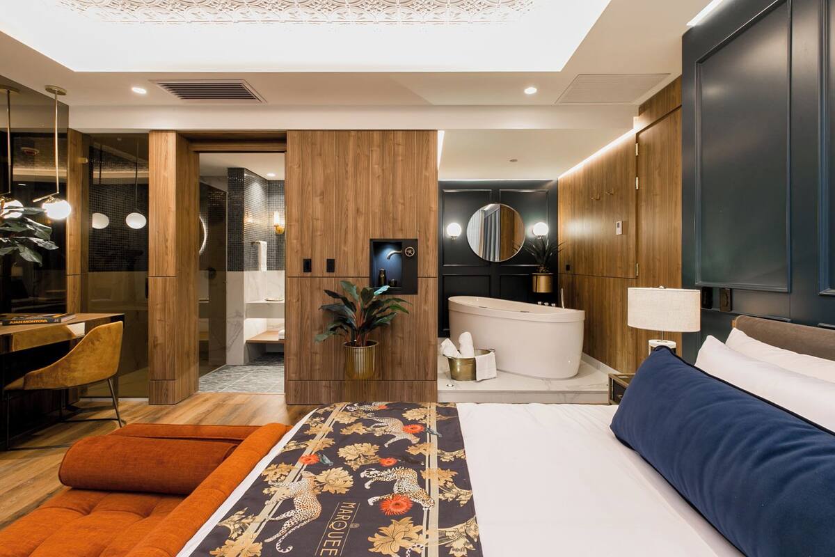 A modern hotel room with a large bed, a desk, a chair, a bathroom with a bathtub, and a mirror.