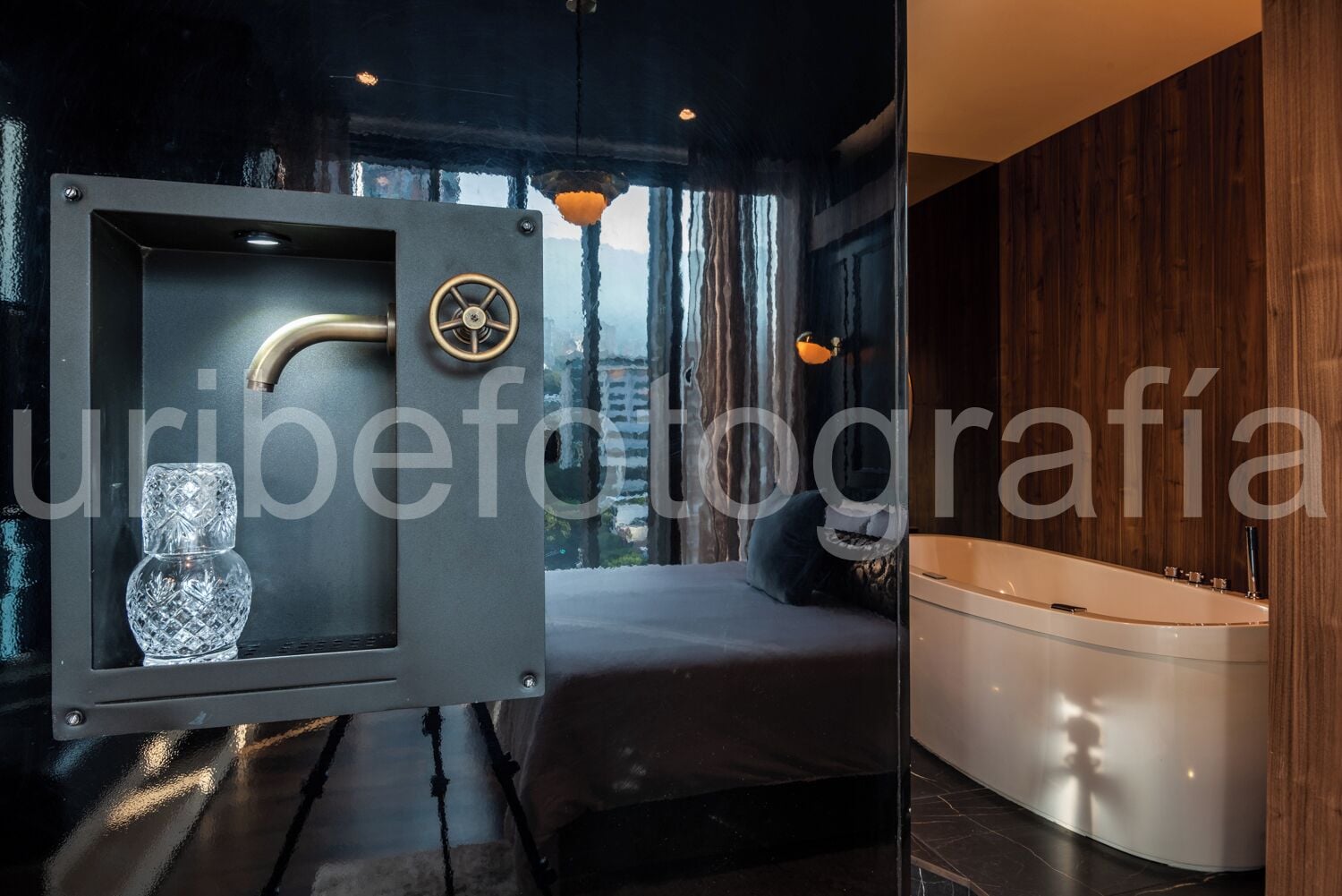 A modern bathroom with a bathtub, a glass-enclosed safe, and a view of the cityscape through large windows.