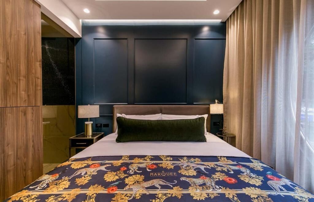 Ein Schlafzimmer mit einem Bett, einem dunklen Holzschrank, einem Nachttisch und einem Fenster mit Vorhängen.