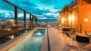 Un área de piscina en la azotea con vista a la ciudad, mobiliario exterior y un muro de ladrillo.