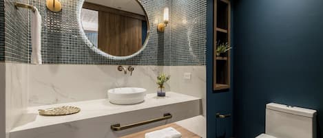 A modern bathroom with a round mirror, white sink, and a wooden vanity.