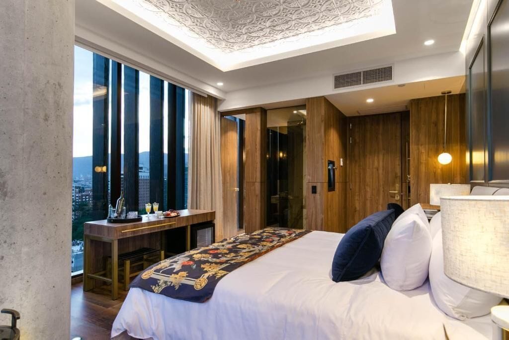 A modern hotel room with a large bed, a desk, and a view of the city.