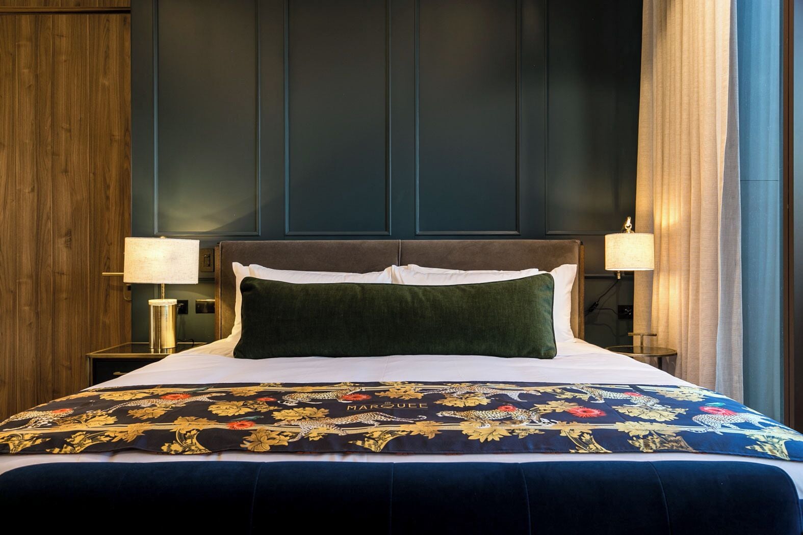 A hotel room with a large bed, dark wood paneling on the walls, and two bedside lamps.