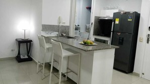 A compact kitchen with a central island, white bar stools, a black refrigerator, and a small side table. - 1ME2 Apartamento en Morros Frente al Mar (Cartagena)