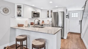 A modern kitchen with white cabinets, stainless steel appliances, a marble countertop, and two bar stools. - Picturesque, High End Vaca Condo, Atlantic Views from all corners. Sunset Deck  (St. Augustine)