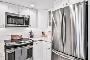 A modern kitchen with stainless steel appliances, white cabinetry, and a wooden cutting board on the countertop.