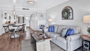 A modern living room with a white sofa, wooden coffee table, and a dining area with a white table and chairs. - Picturesque, High End Vaca Condo, Atlantic Views from all corners. Sunset Deck  (St. Augustine)
