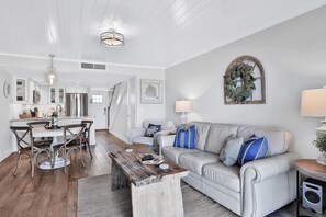 A modern living room with a white sofa, wooden coffee table, and a dining area with a white table and chairs. - Picturesque, High End Vaca Condo, Atlantic Views from all corners. Sunset Deck  (St. Augustine)
