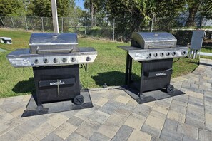 Two portable gas grills labeled 'NEXGRILL' on a paved patio with a grassy area and a fence in the background.
