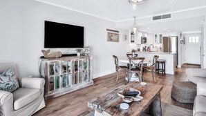 A modern living room with a wooden coffee table, white sofas, and a dining area with chairs and a table. - Picturesque, High End Vaca Condo, Atlantic Views from all corners. Sunset Deck  (St. Augustine)