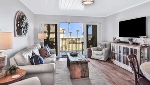 A modern living room with a sofa, coffee table, TV, and a view to the outside. - Picturesque, High End Vaca Condo, Atlantic Views from all corners. Sunset Deck  (St. Augustine)