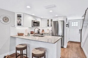 Una cocina moderna con armarios blancos, electrodomésticos de acero inoxidable e isla de mármol con dos taburetes.
