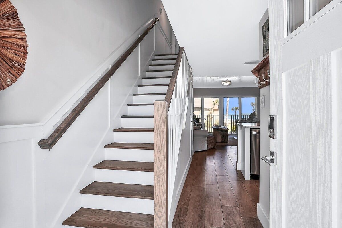 A staircase with wooden steps and a handrail, leading to a kitchen area with modern appliances and a view of the outdoors.