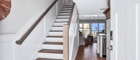 A staircase with wooden steps and a handrail, leading to a kitchen area with modern appliances and a view of the outdoors.