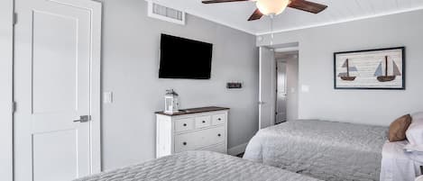 Un dormitorio con dos camas, ventilador de techo, televisión, cómoda y un cuadro en la pared.