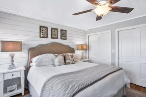 A bedroom with a bed, nightstands, a ceiling fan, and framed pictures on the wall.