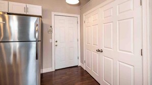 Una cocina con un refrigerador de acero inoxidable, armarios blancos y piso de madera.