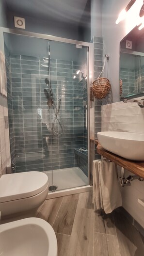 Un bany modern amb dutxa envidriada, vàter blanc i un lavabo amb taulell de fusta.