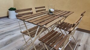 Een houten inklapbare tafel met stoelen in een binnenplaats, met een beige muur en een raam.