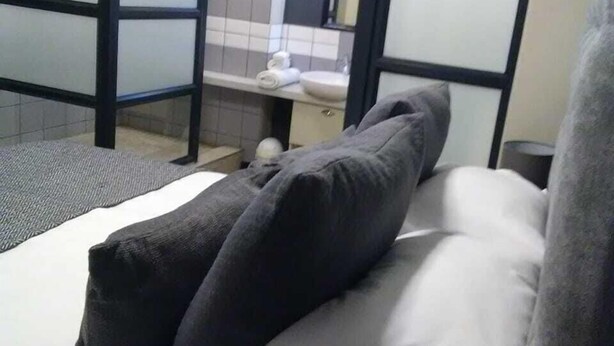 A hotel room with a bed, a small bathroom with a toilet and sink, and a shower area. - Rose Of Rose (Johannesburg)
