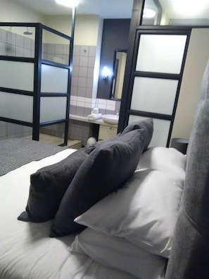 A hotel room with a bed, a small bathroom with a toilet and sink, and a shower area.