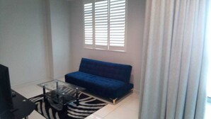 A living room with a blue sofa, a glass coffee table, and a zebra-patterned rug. - Rose Of Rose (Johannesburg)