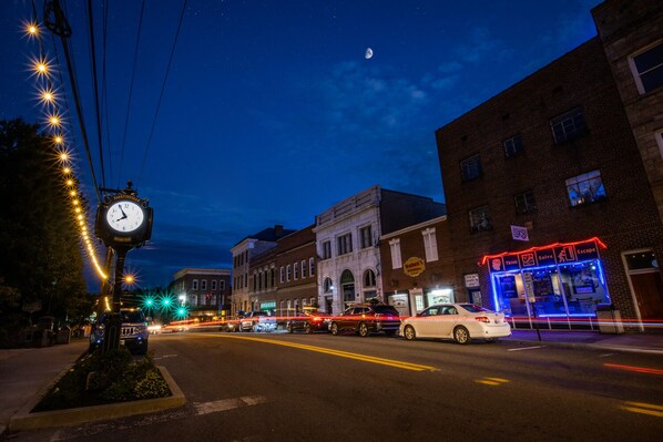 A street scene at night with a clock, buildings, and a neon-lit establishment.