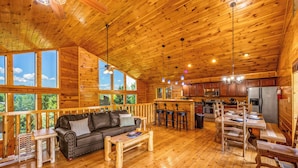 A spacious wooden cabin with a living area, kitchen, and large windows offering views of the outdoors.