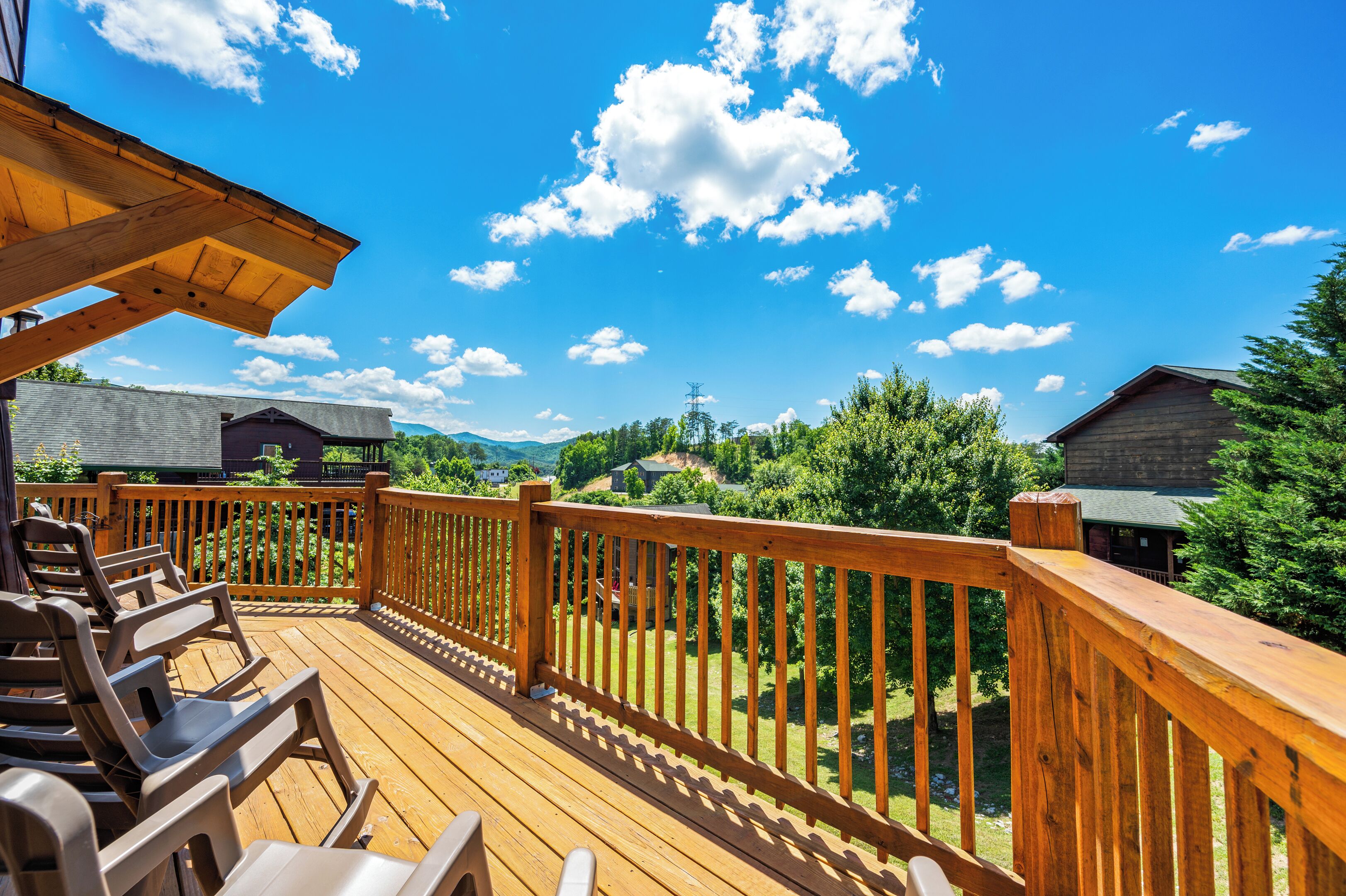 A wooden deck with chairs, a railing, and a view of a forest and mountains.