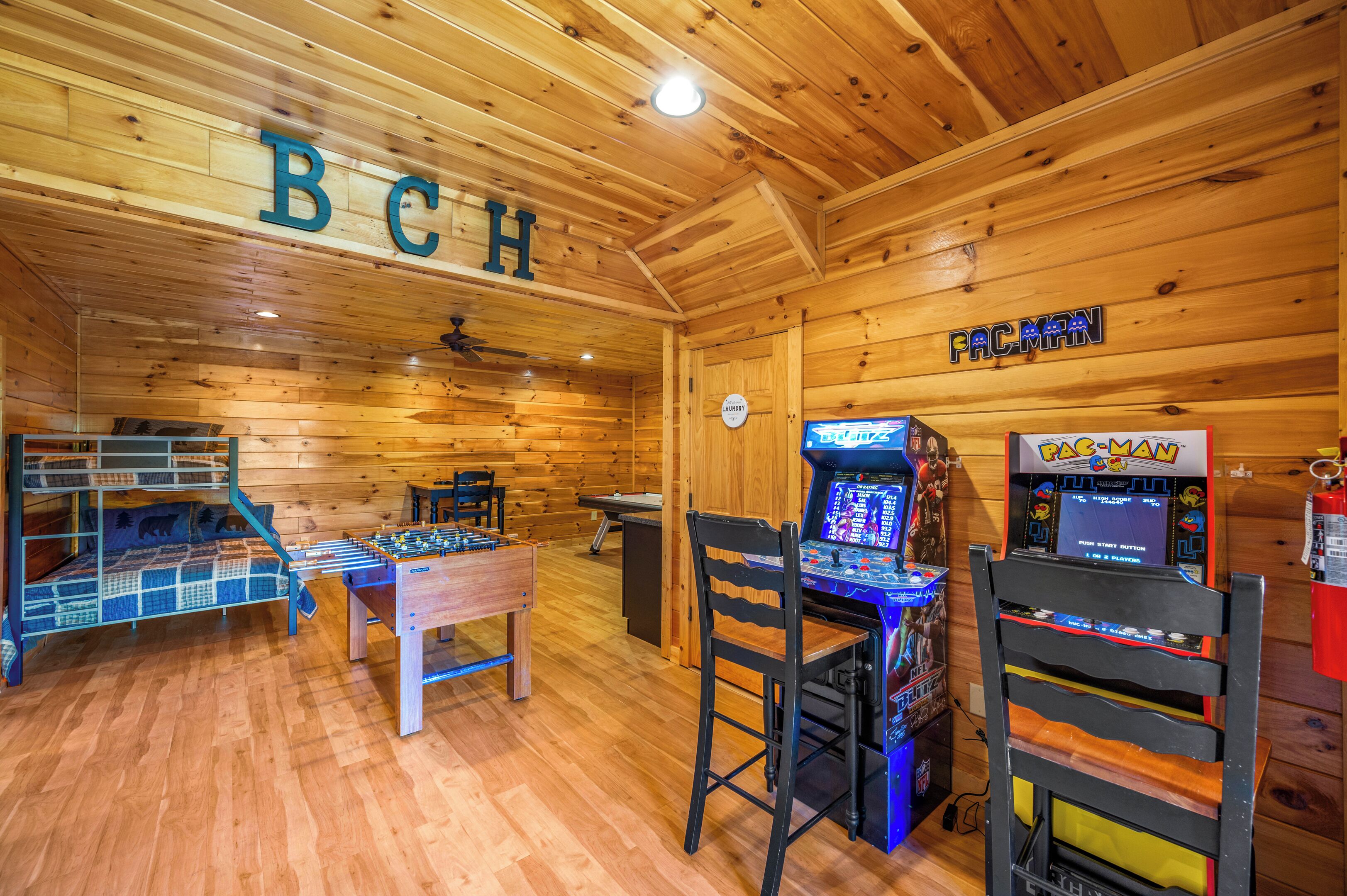 A wooden interior with a foosball table, a pool table, and two arcade machines.