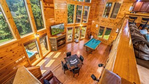 A wooden cabin interior with a pool table, billiards, and a fireplace.