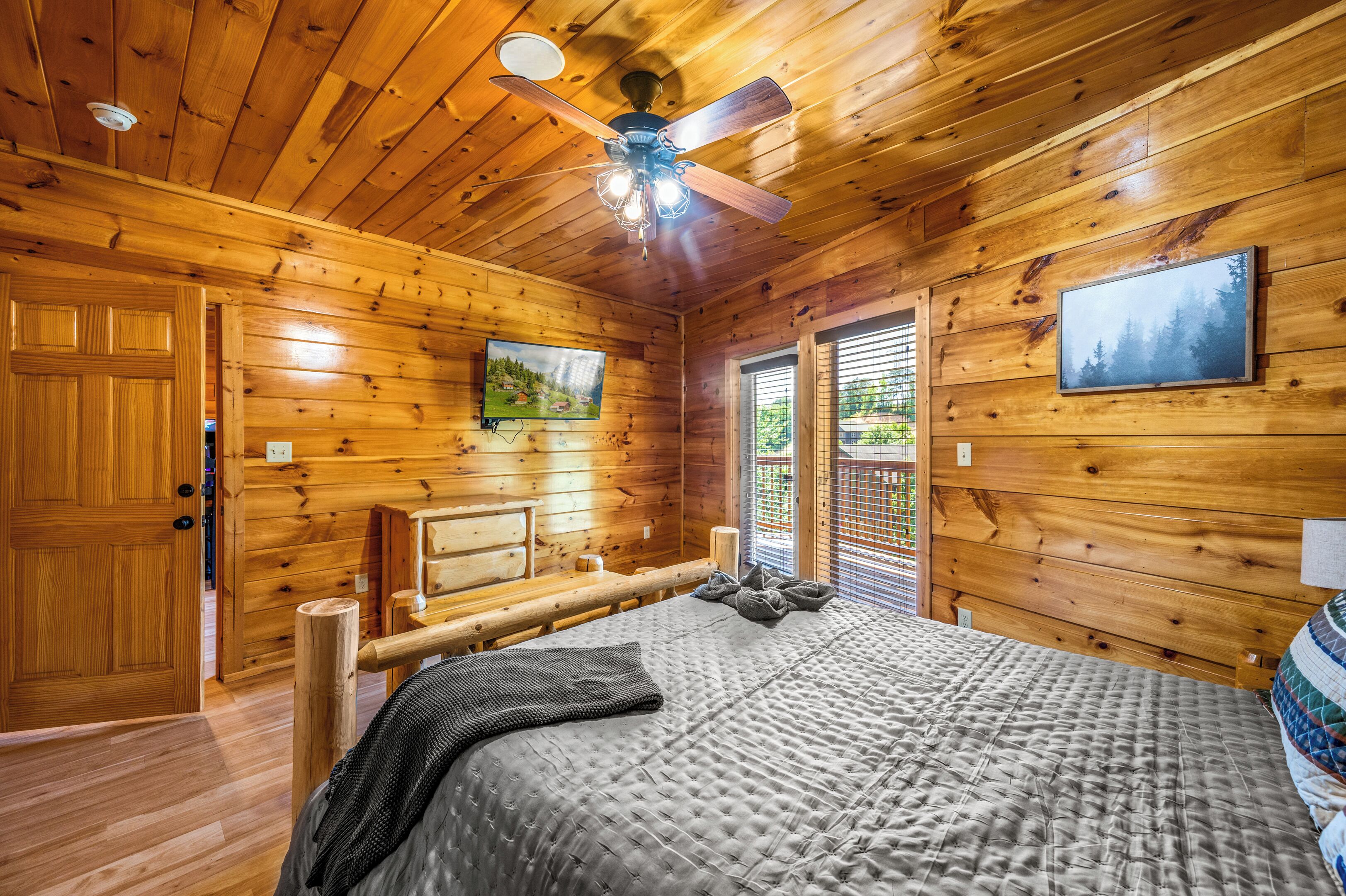 A wooden cabin bedroom with a bed, ceiling fan, and two framed pictures on the walls.