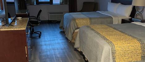 A hotel room with two beds, a desk with a computer, a chair, a window with curtains, and a lamp.