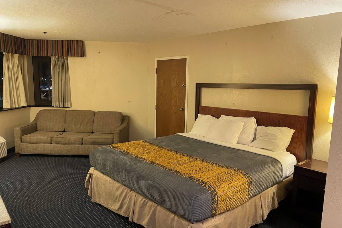 A hotel room with a large bed, a sofa, a wooden door, and a window with curtains.
