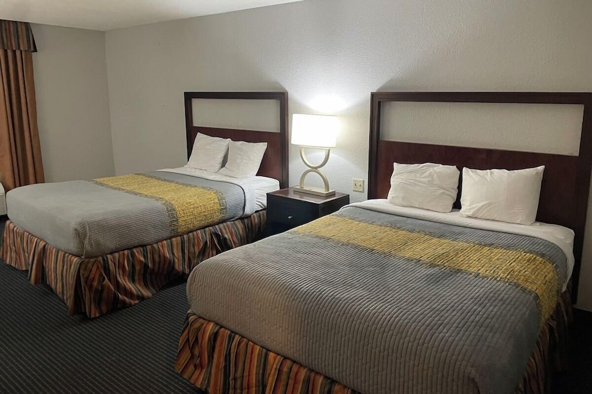 A hotel room with two beds, each with a headboard, a bedside table, and a lamp.