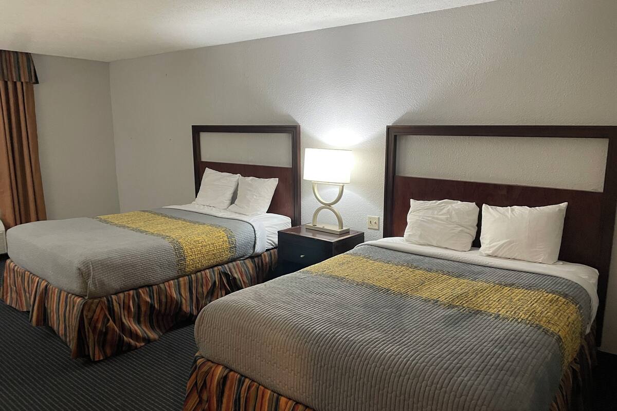 A hotel room with two beds, each with a wooden headboard, a bedside table with a lamp, and striped bedding.
