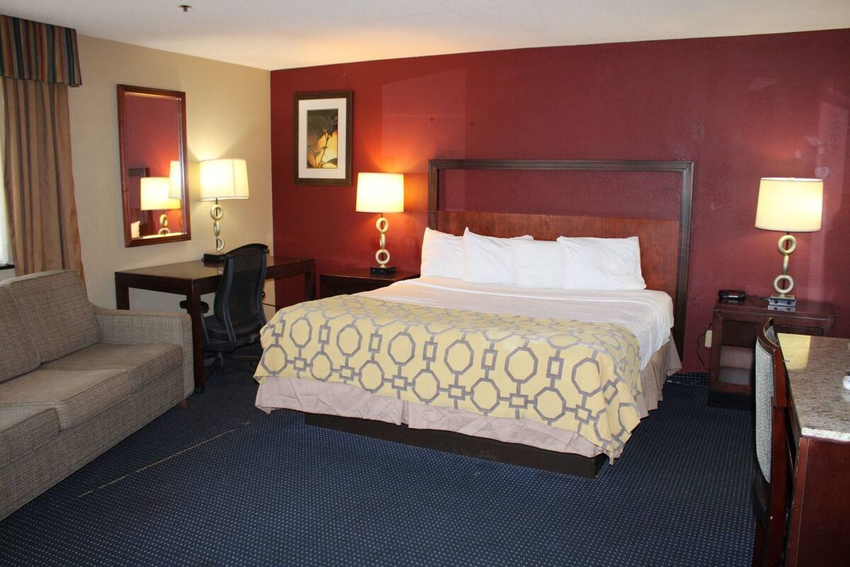 A hotel room with a bed, a sofa, a desk, and two lamps.